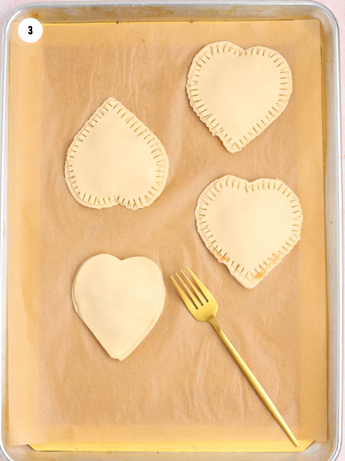 Crimping the edges of heart-shaped hand pies with a fork to seal the filling.