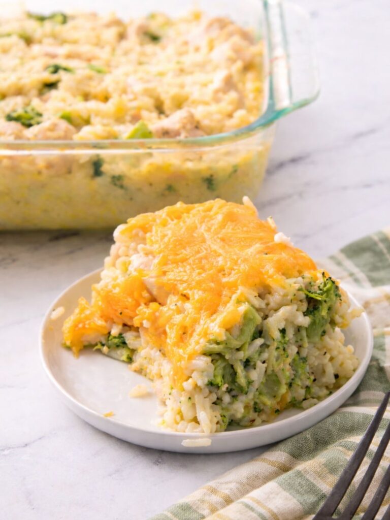 White plate with a serving of Chicken Rice Casserole with Broccoli. Casserole dish in the background.