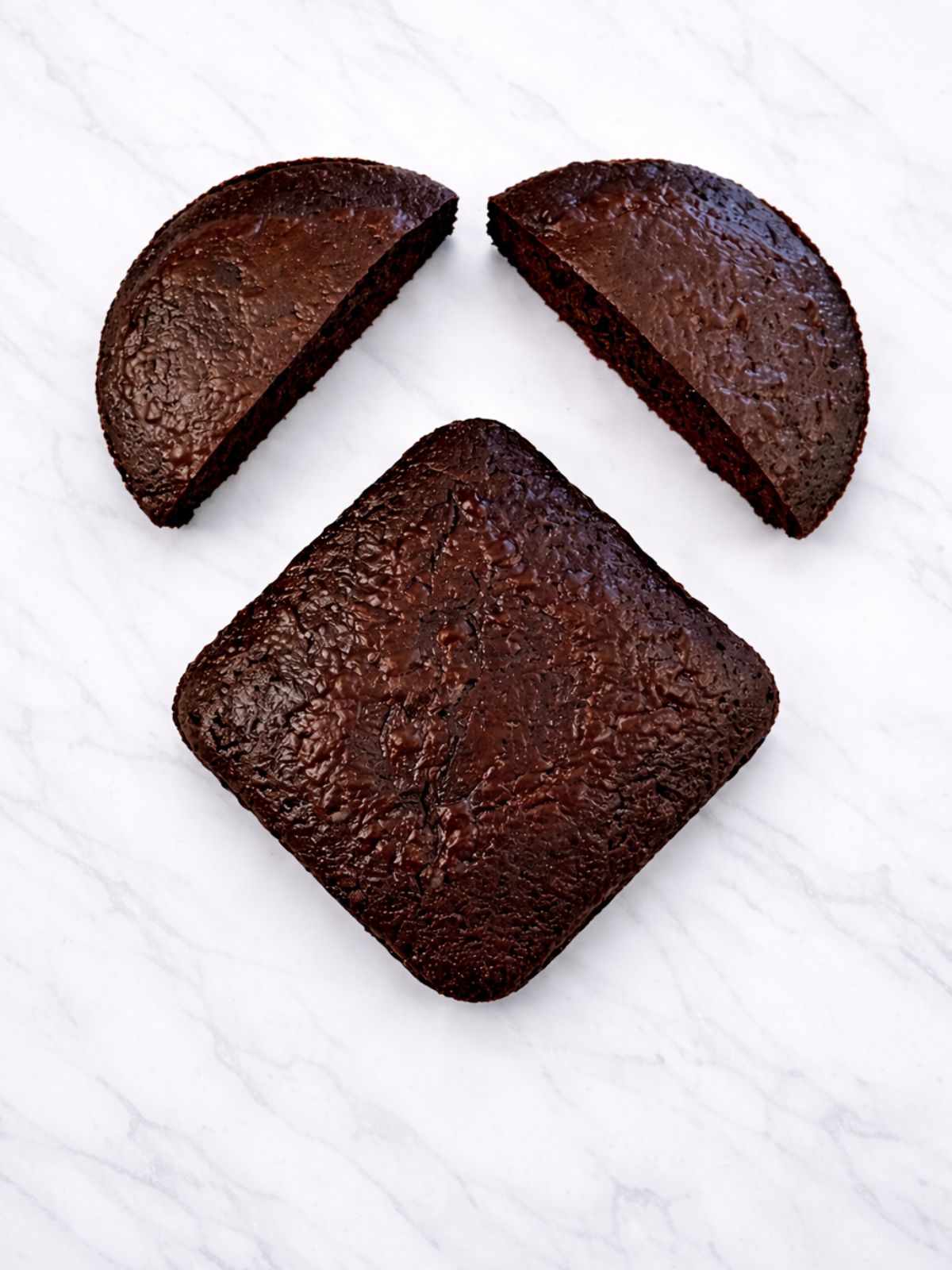 round chocolate cake cut into two pieces above square chocolate cake set as a diagonal.