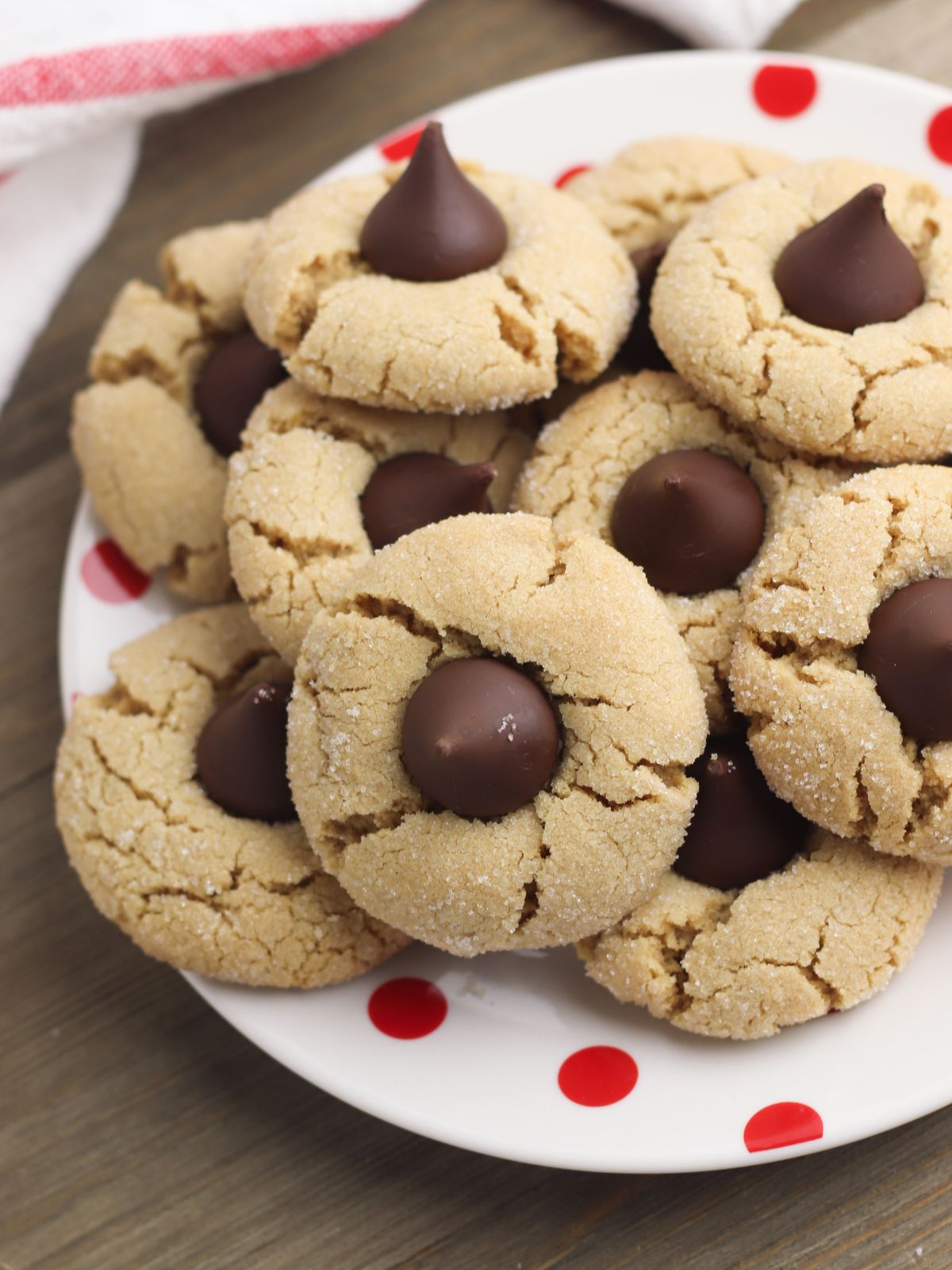 Peanut Butter Blossoms Cookies - soft, chewy cookies with a sugary coating topped with everyone's favorite chocolate candy kiss from Walking on Sunshine Recipes. peanut butter blossom cookies on plate with red dots.