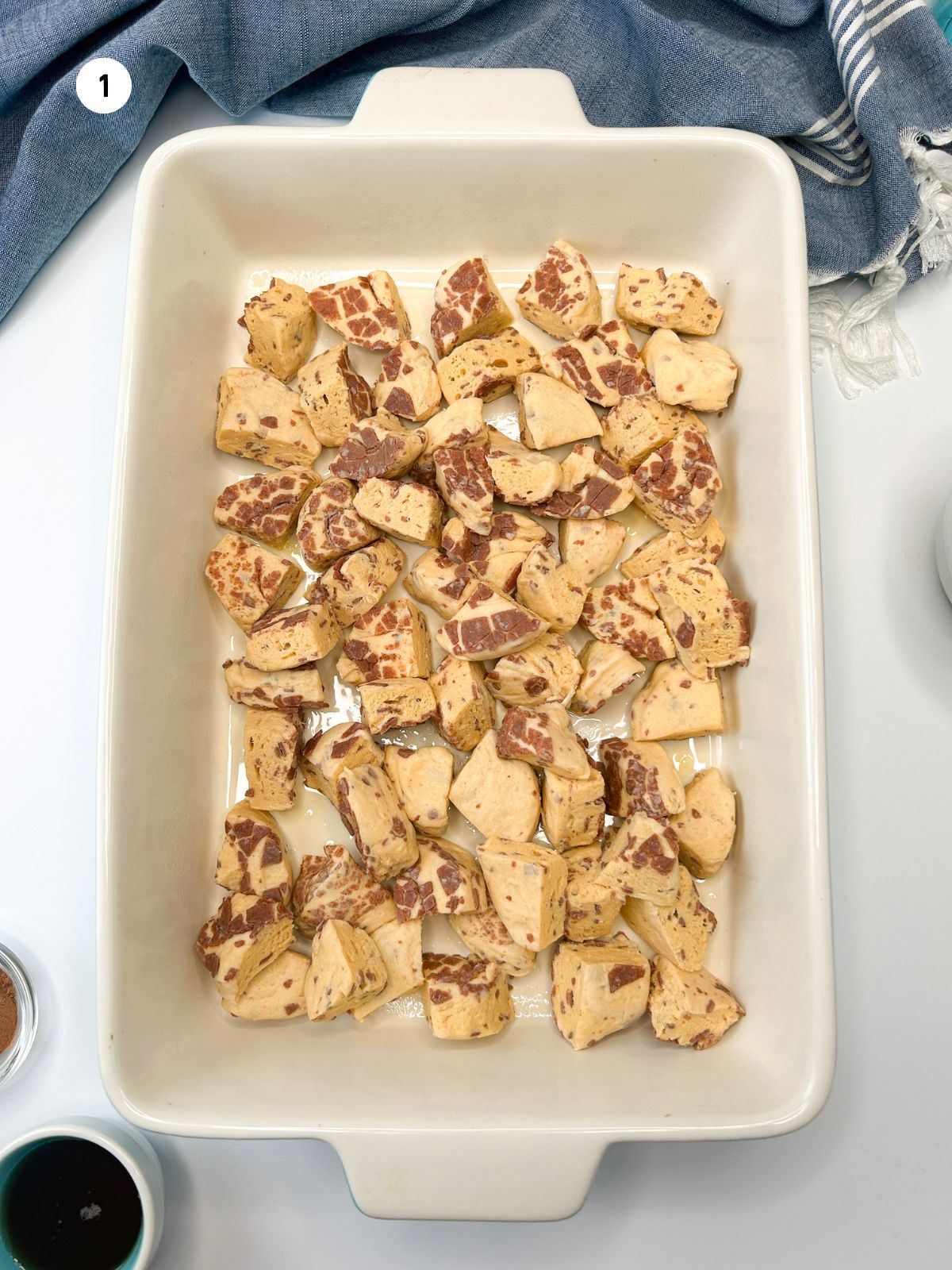 cut up pieces of refrigerated cinnamon rolls spread around in large casserole dish.