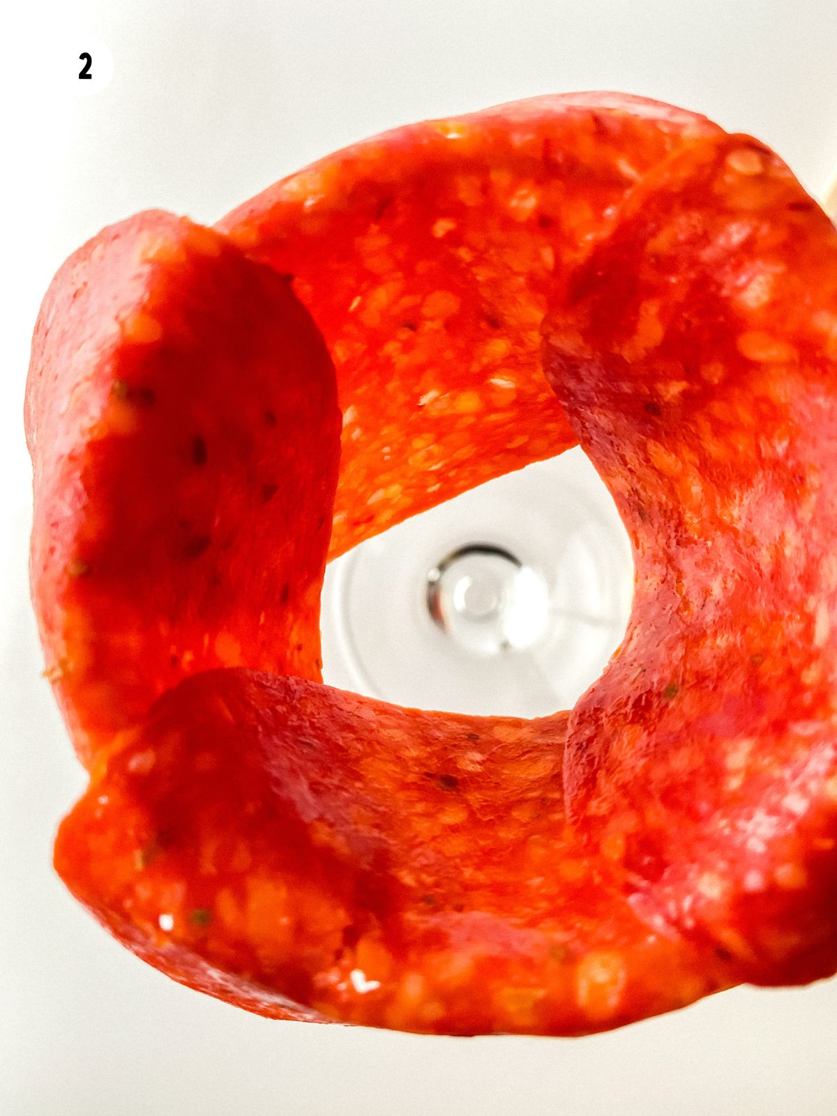 Adding more layers of pepperoni around a glass to shape a pepperoni rose step by step.