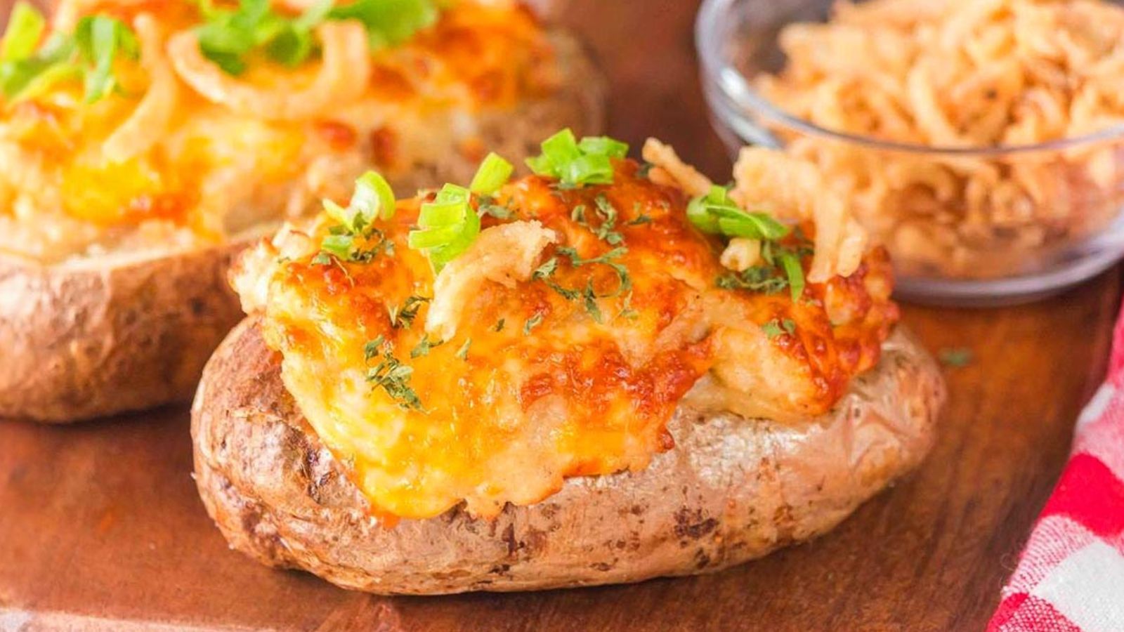 Two halved potatoes topped with melted cheese and browned onions are arranged on a plate.