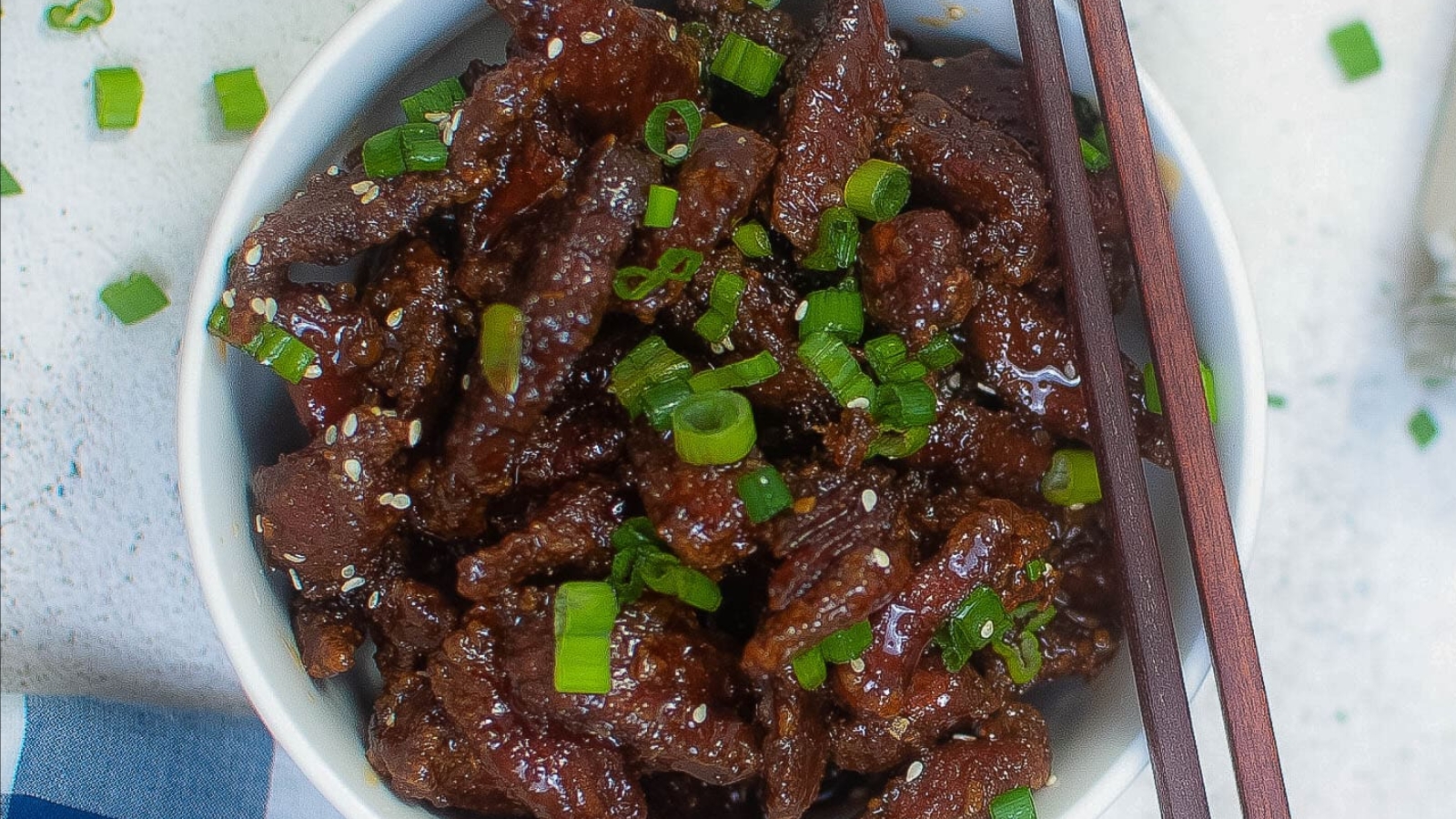 Closeup of crispy beef in a bowl with green onions and sesame seeds.