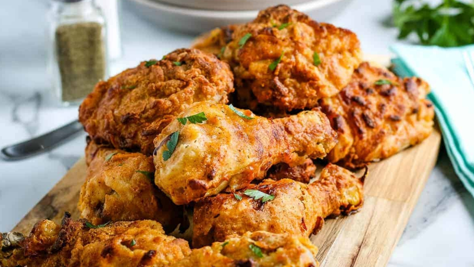 Air fryer fried chicken legs and thighs in a pile on a wooden cutting board.