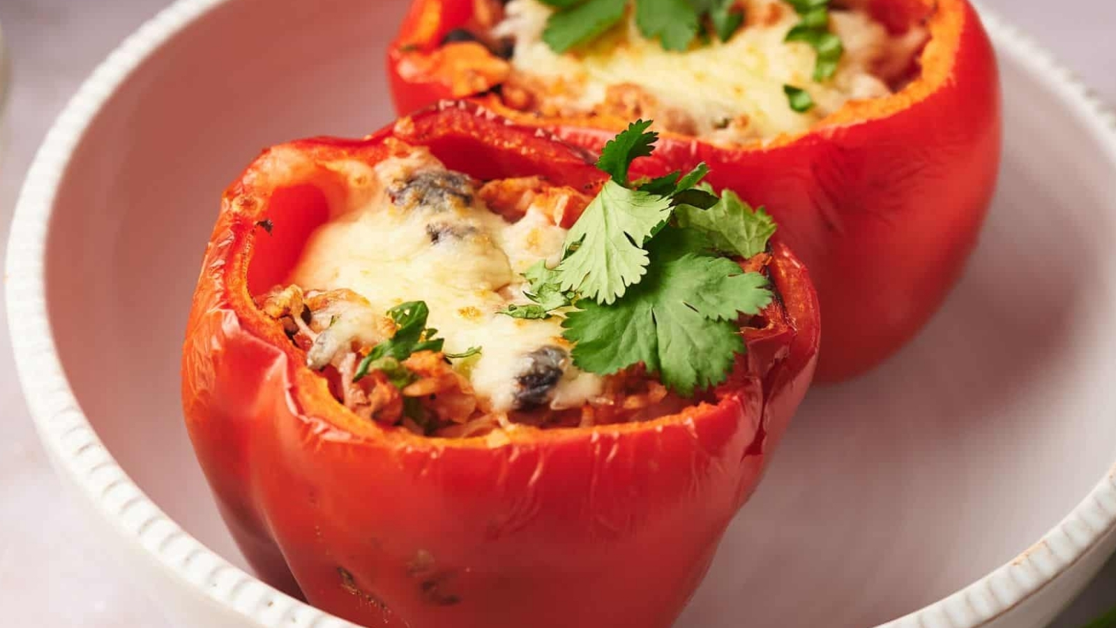 Two stuffed peppers in a bowl with melted cheese on top.