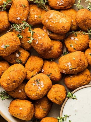 A plate full of sweet potato tater tots with dip.