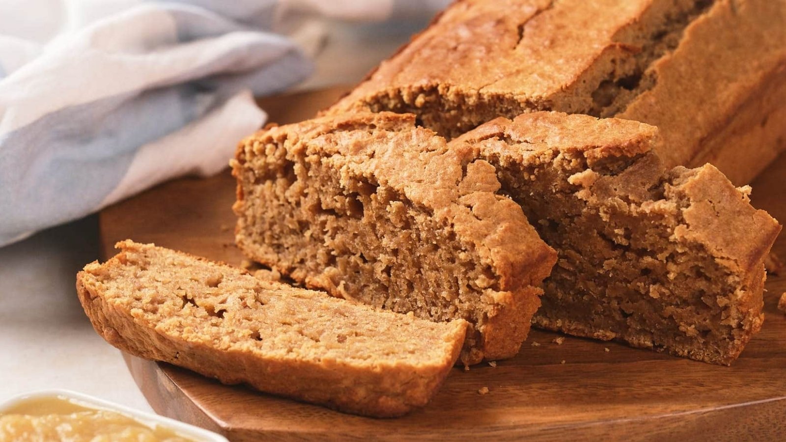 A loaf of applesauce bread with a few slices cut, displayed on a wooden board.