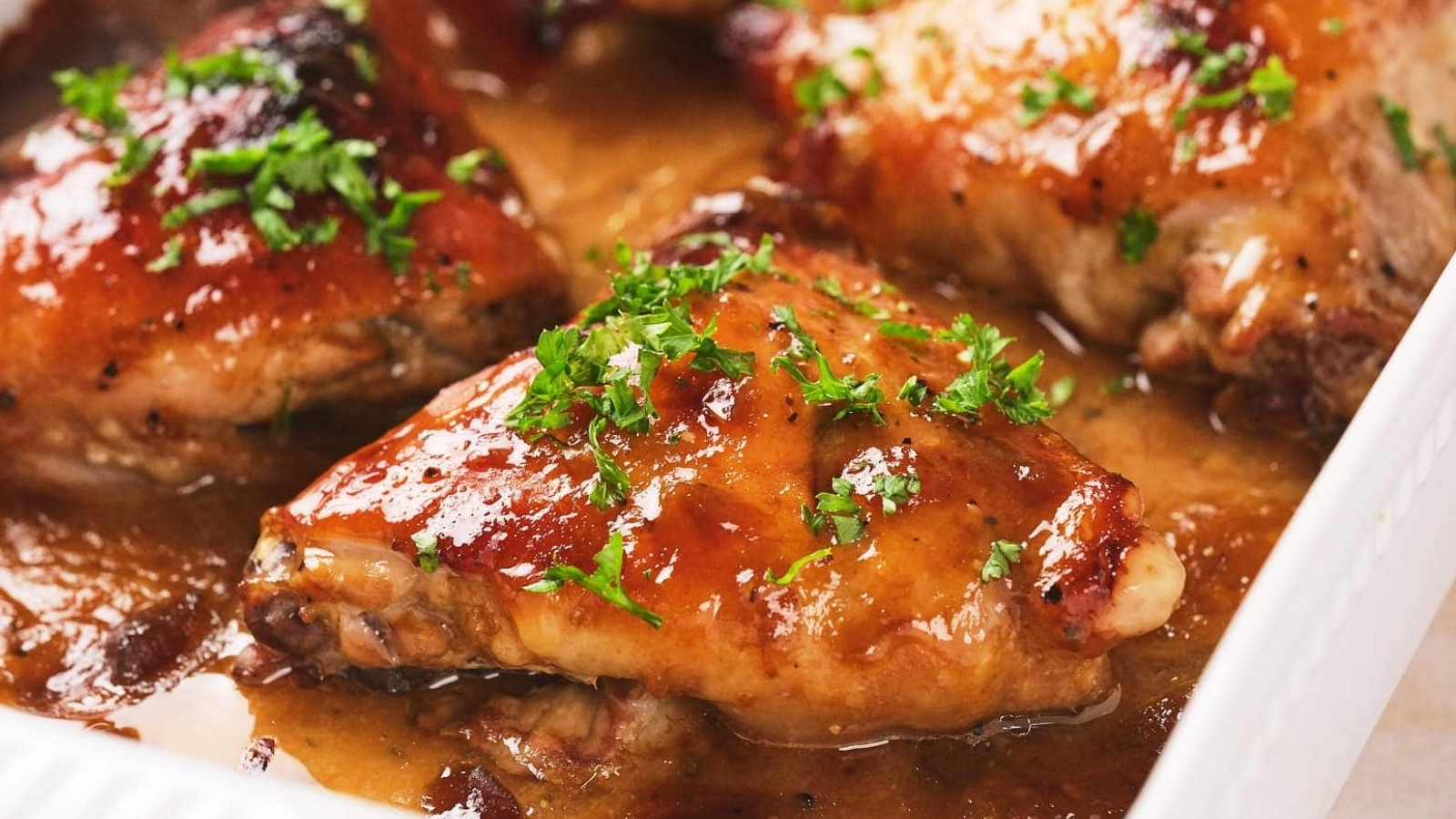 Baked apricot chicken with a golden glaze, garnished with chopped parsley, served in a white dish.