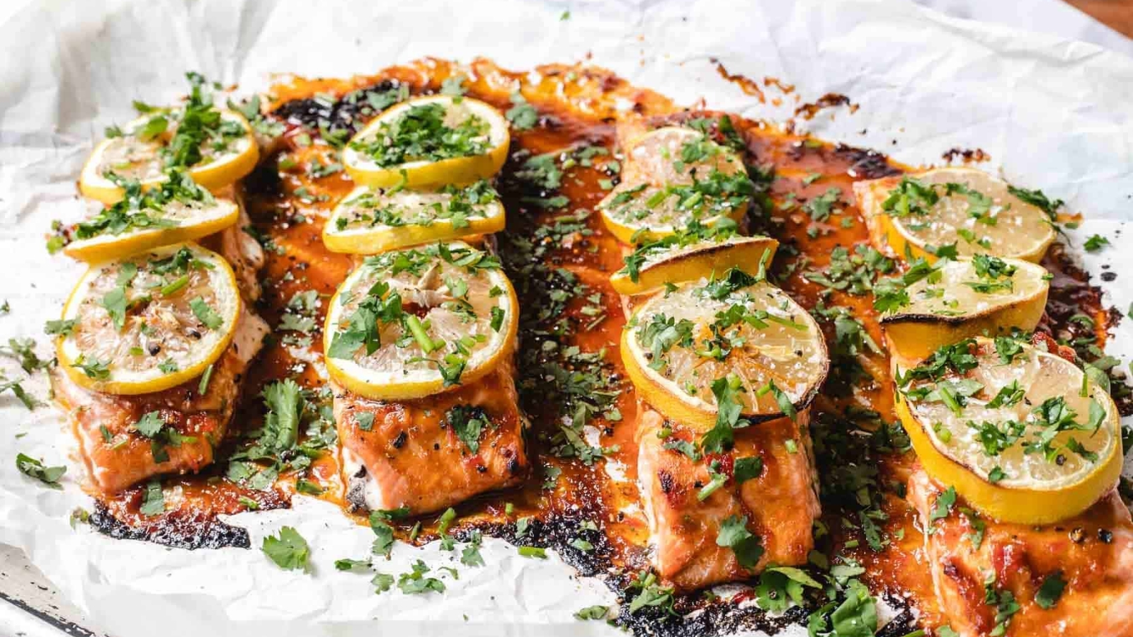 Baked salmon fillets topped with lemon slices and fresh herbs on a sheet of parchment paper.