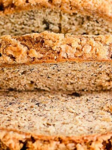 Sliced banana bread with a crumbly topping on a wooden cutting board.
