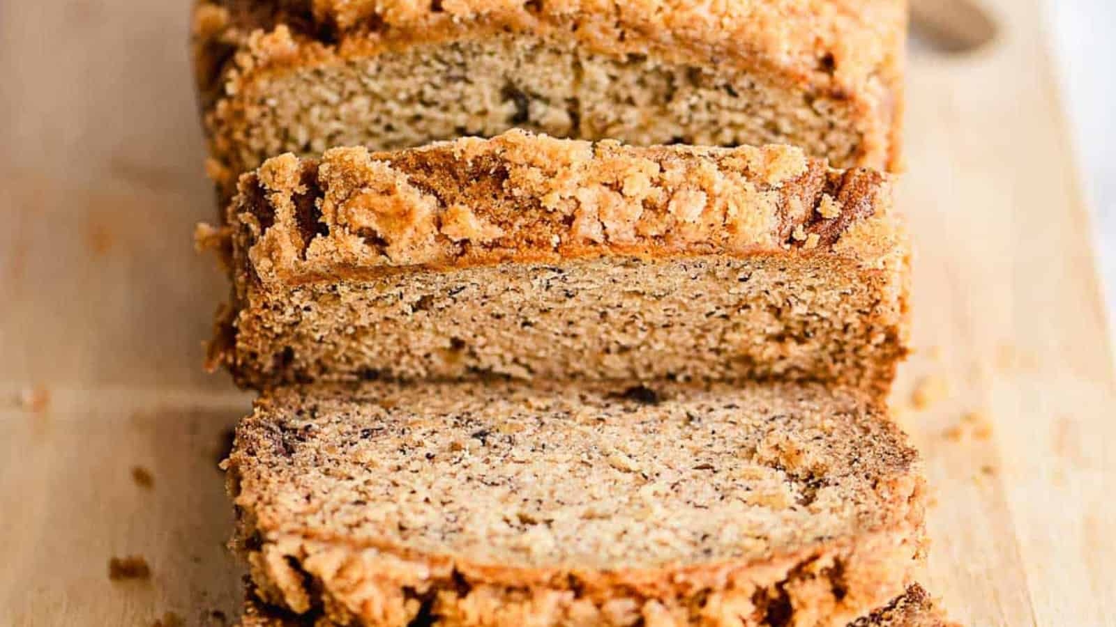 Sliced banana bread with a crumbly topping on a wooden cutting board.