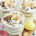 Close-up of an individual Easter banana pudding parfait with layered vanilla pudding, cookies, banana slices, and chocolate candy toppings.