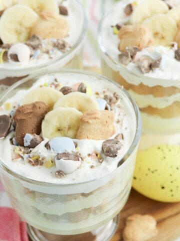 Close-up of an individual Easter banana pudding parfait with layered vanilla pudding, cookies, banana slices, and chocolate candy toppings.