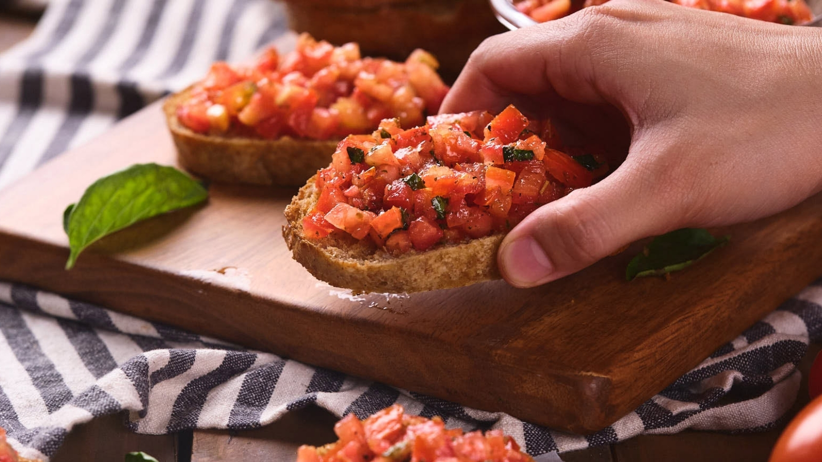 A person's hand picking up a slice of bruschetta al pomodoro.