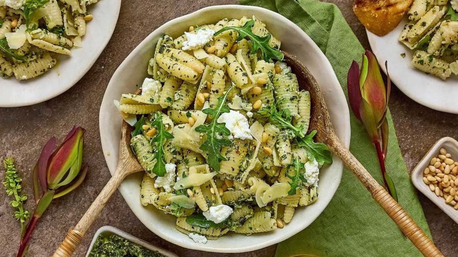 Cavatelli pasta tossed with green pesto and ricotta in a bowl with pine nuts and scattered arugula leaves.