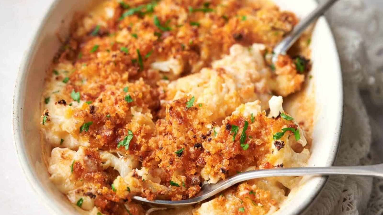 Cheesy cauliflower casserole in a white dish with spoons.