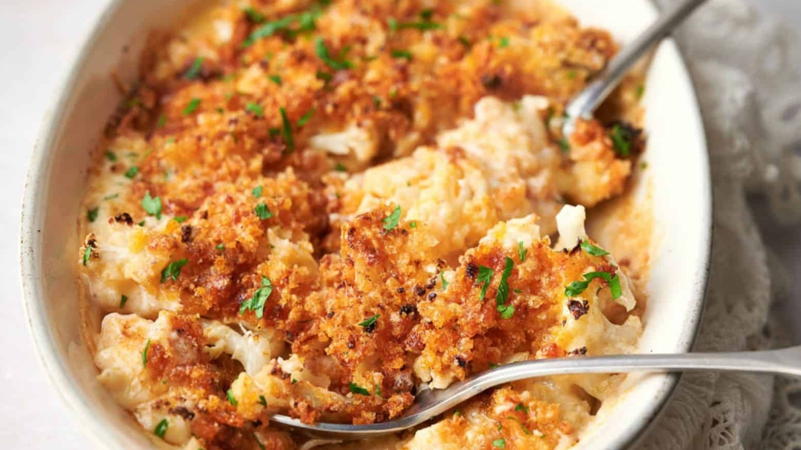 Cheesy cauliflower casserole in a white dish with spoons.