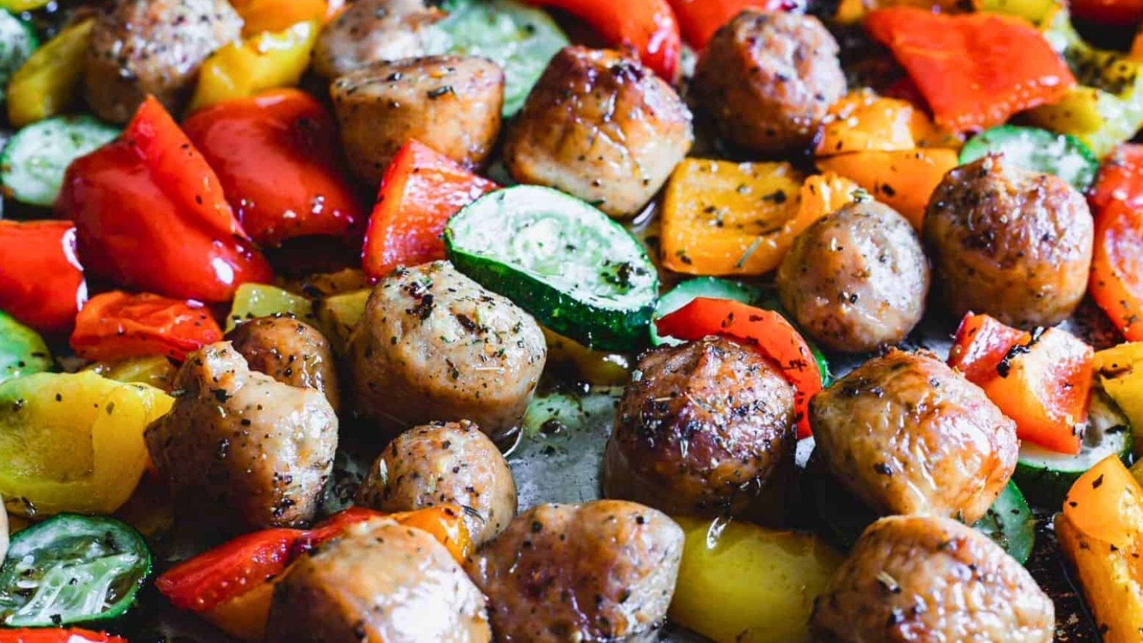 Close-up of roasted meatballs with a mix of colorful, chopped bell peppers and zucchini slices.