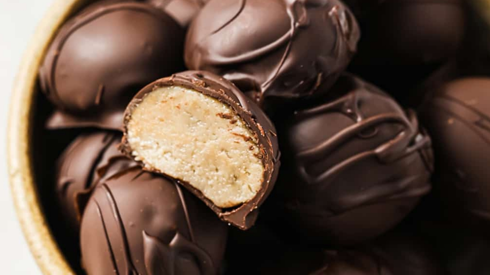 A bowl of chocolate-covered peanut butter balls with one cut in half.
