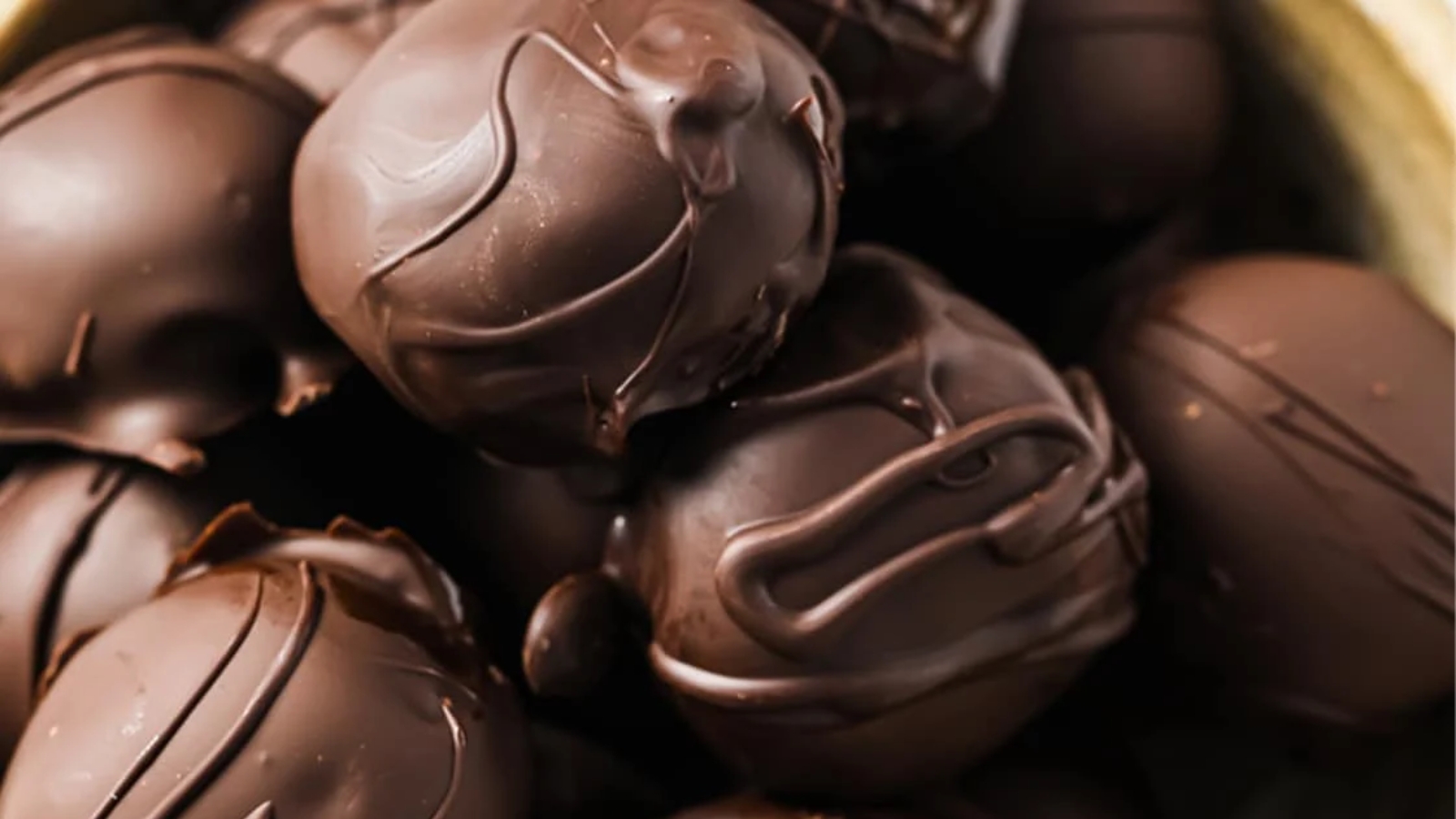 A bowl of chocolate-covered peanut butter balls with one cut in half.