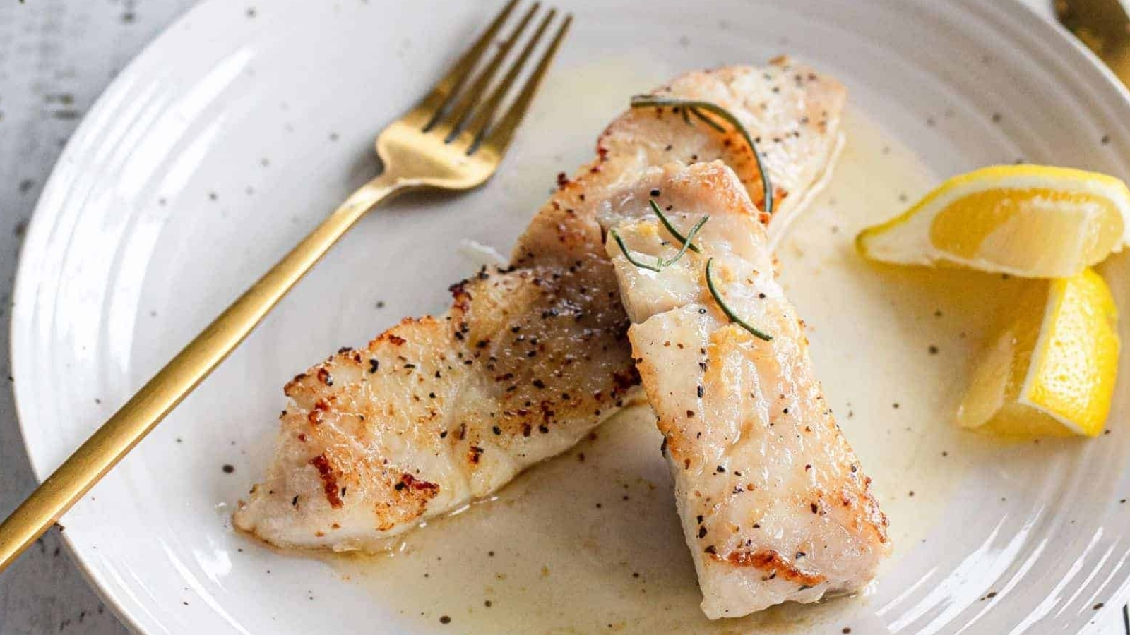 White fish fillets on a white plate with lemon wedges and fork.