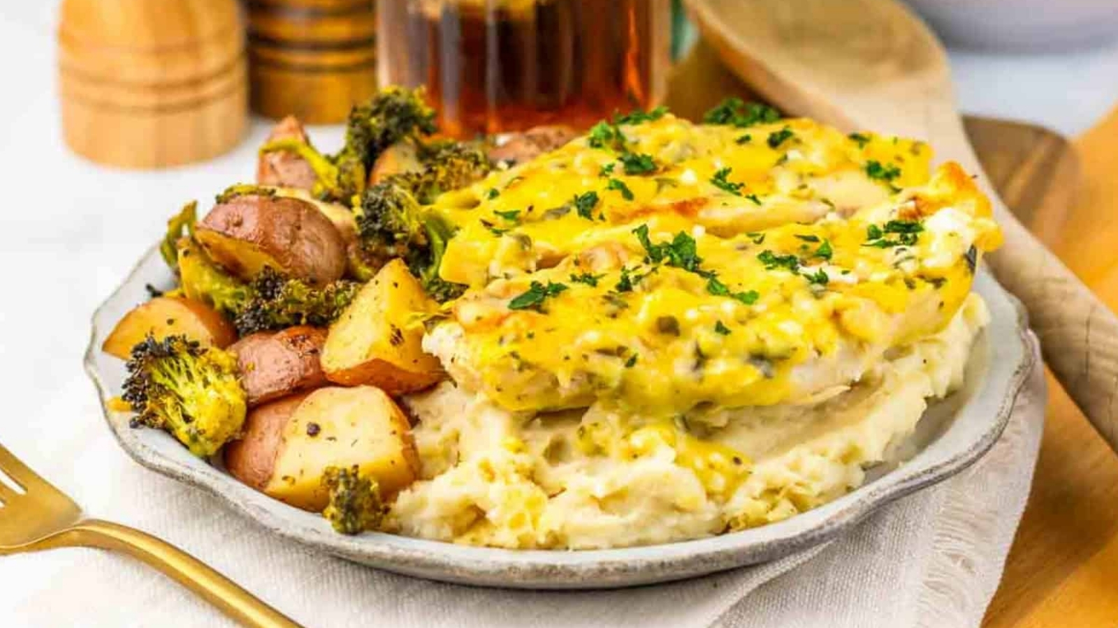 A plate of mashed potatoes, baked chicken with sauce, and roasted potatoes with broccoli, garnished with herbs.