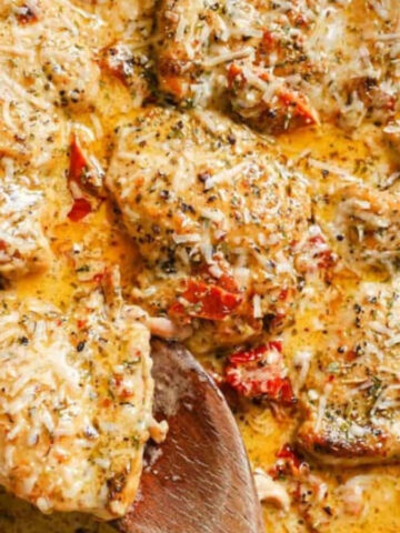A skillet of creamy sun dried tomato chicken with a wooden spoon.