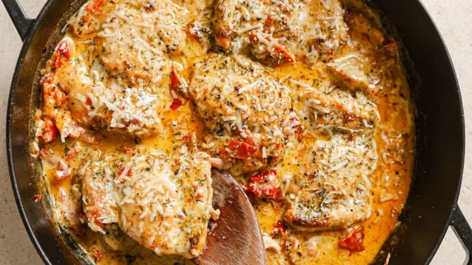 A skillet of creamy sun dried tomato chicken with a wooden spoon.