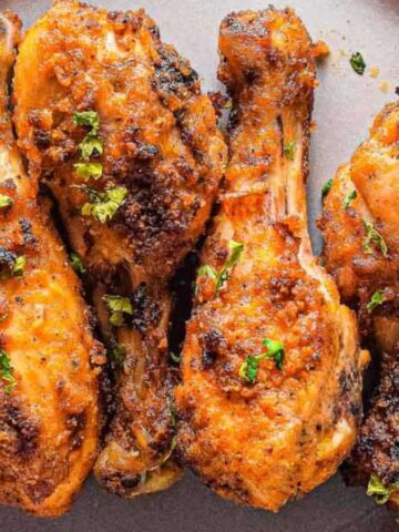 Four chicken drumsticks with parsley on a plate.
