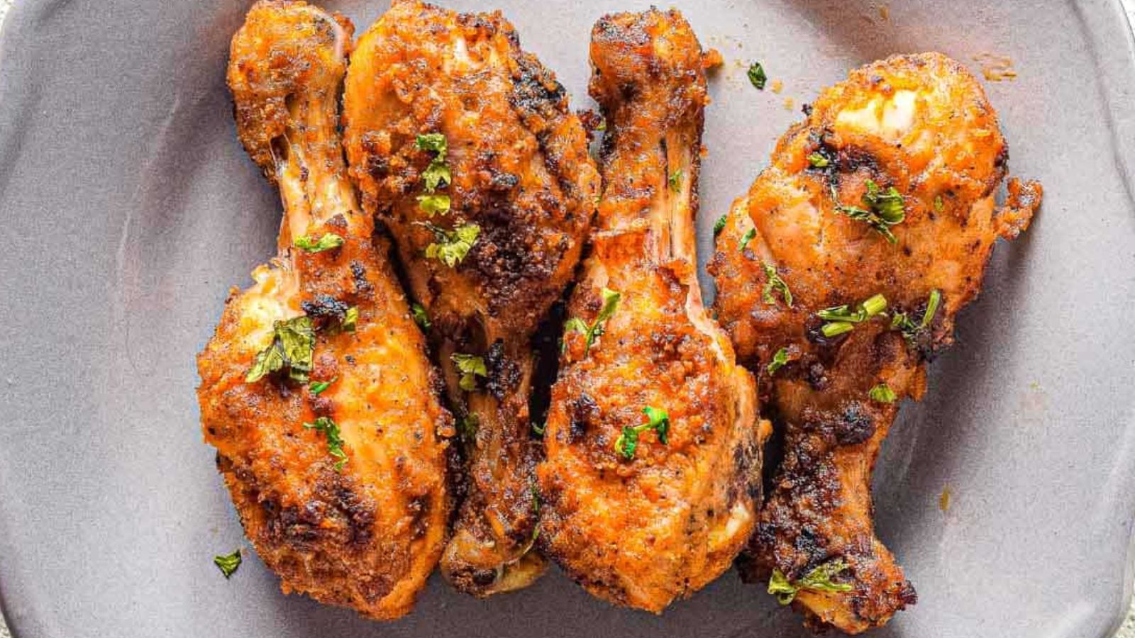 Four chicken drumsticks with parsley on a plate.