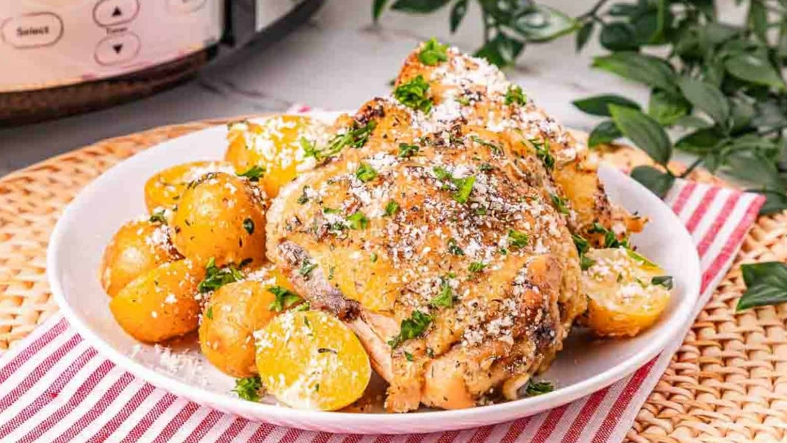 A plate of roasted chicken and baby potatoes, garnished with herbs and grated cheese, on a red-striped napkin.