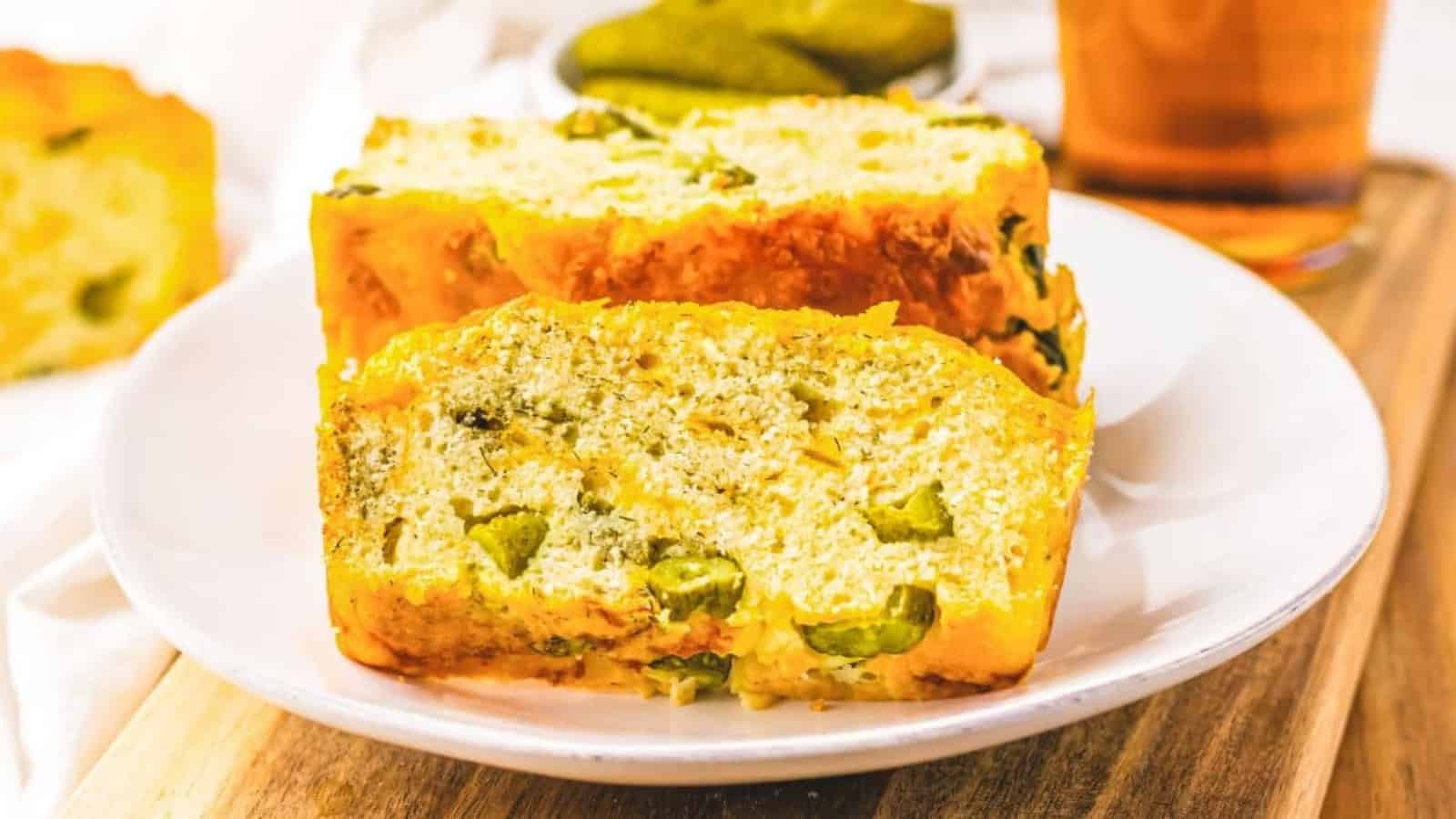 Two slices of savory bread with visible pieces of pickles on a white plate, served on a wooden board.