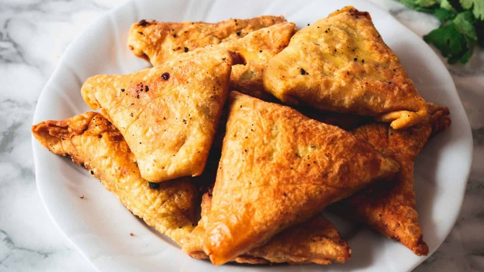 Golden-brown triangular samosas on a white plate.