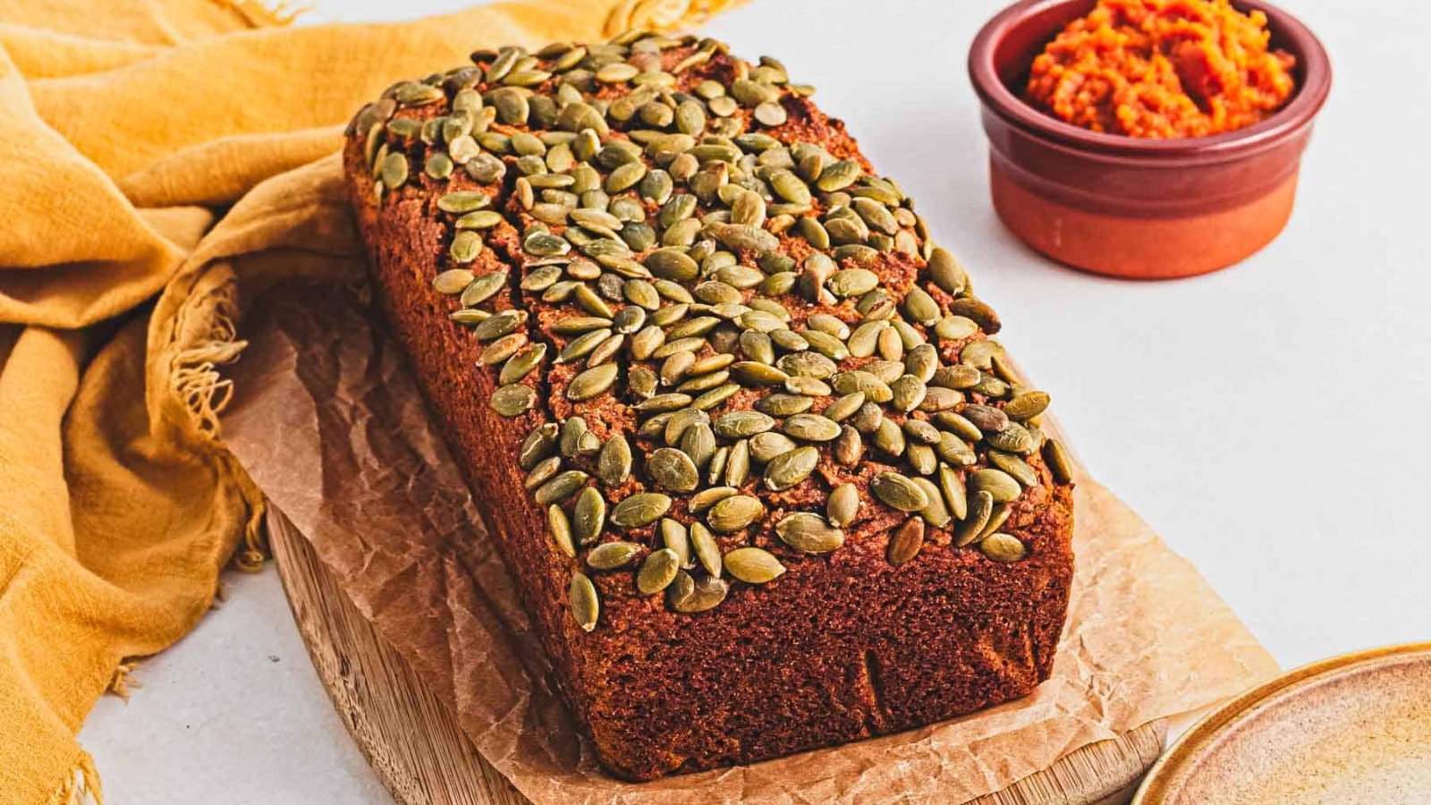 A slice of pumpkin bread on a wooden cutting board.