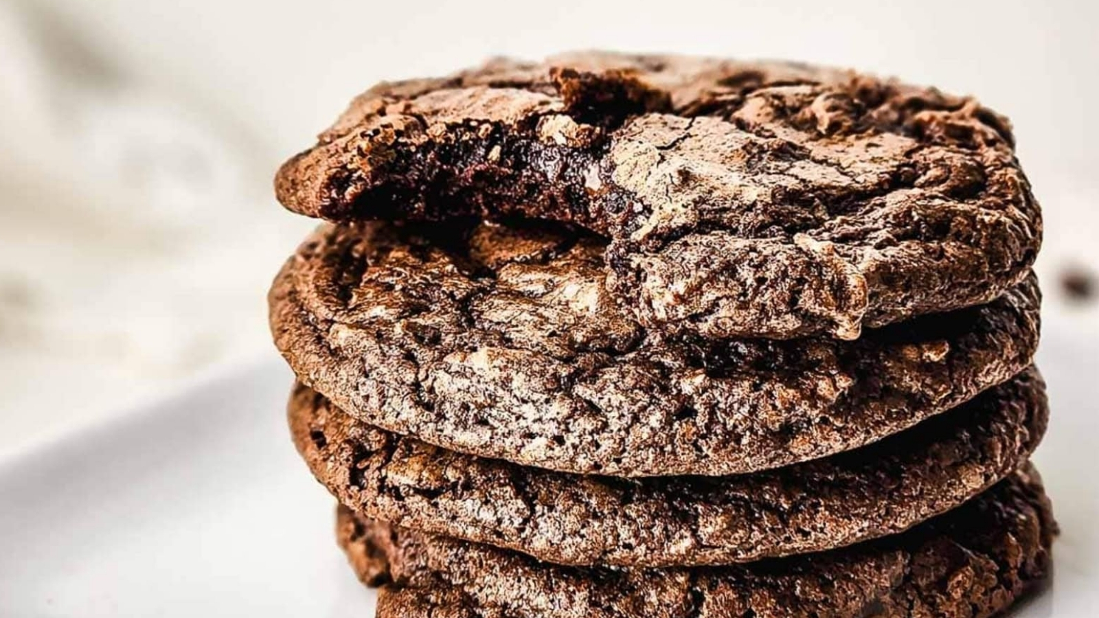 A stack of chocolate cookies, with the top cookie missing a bite, on a white surface.