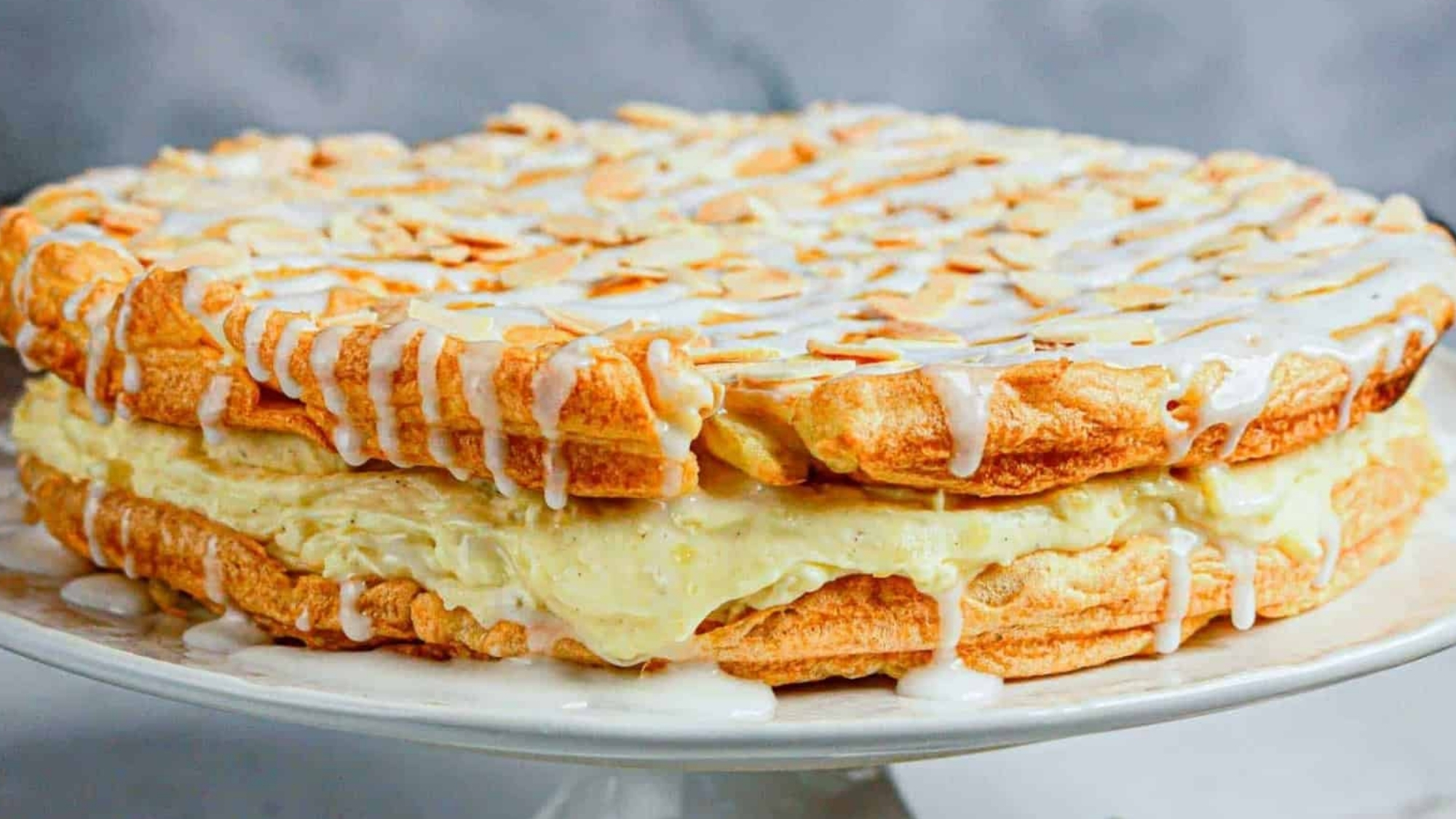 A layered almond pastry cake with cream filling, drizzled with white icing and topped with sliced almonds.