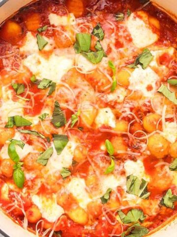 Gnocchi covered in tomato sauce and melted cheese in a shallow baking dish, garnished with basil leaves.