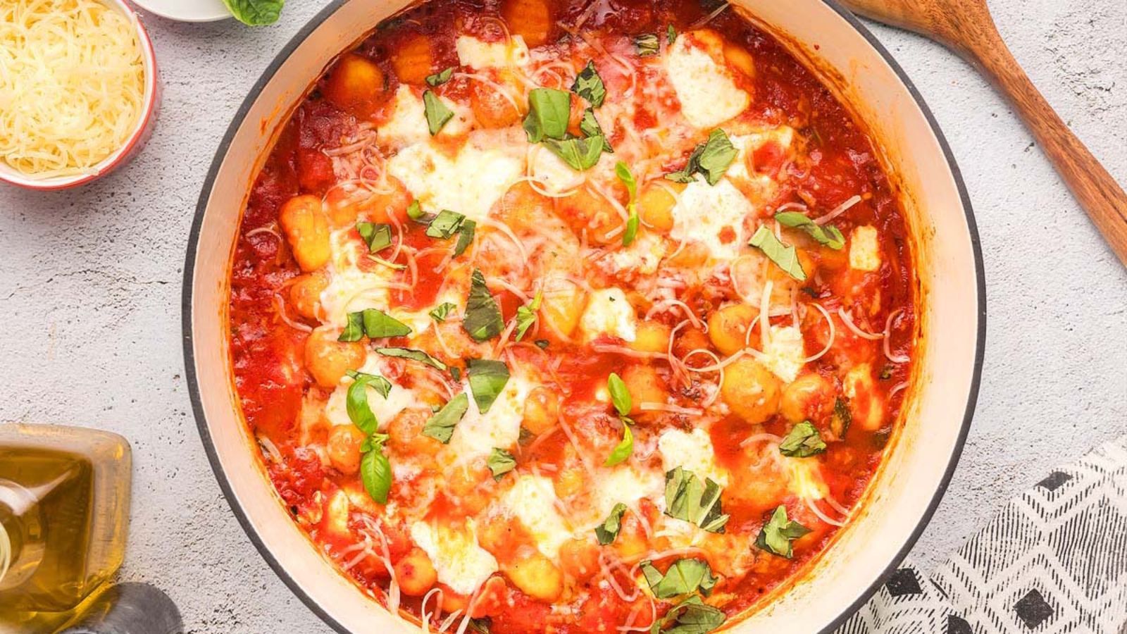 Gnocchi covered in tomato sauce and melted cheese in a shallow baking dish, garnished with basil leaves.
