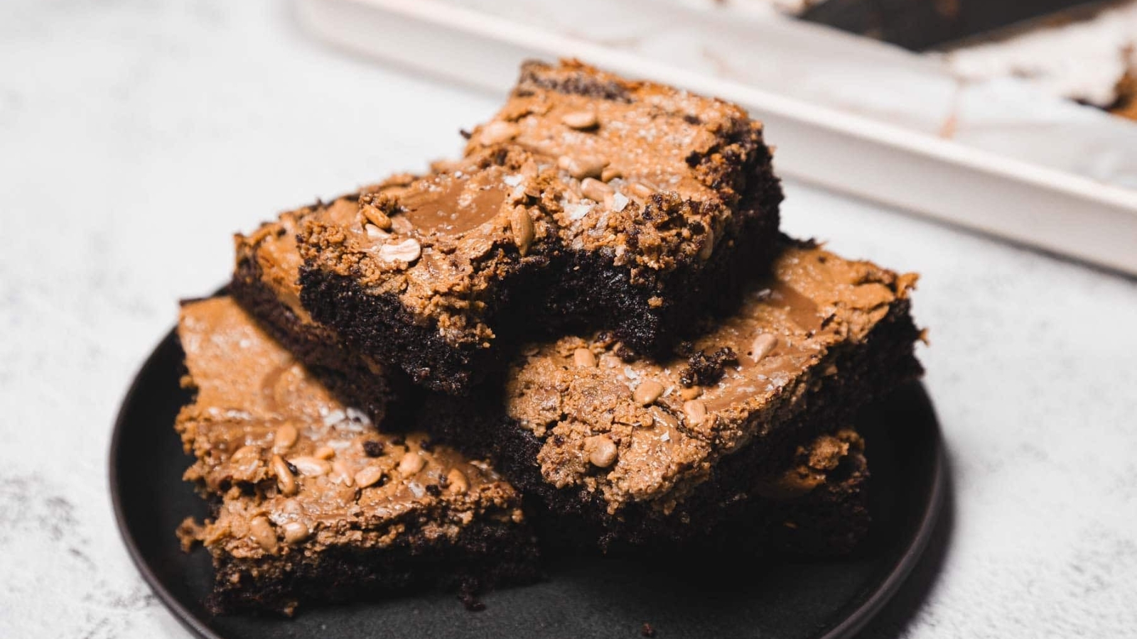 A stack of fudgy chocolate brownies with a cracked top, served on a black plate.