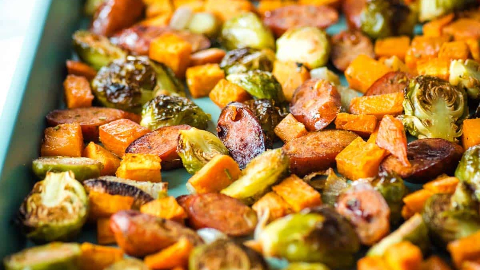 Roasted chicken apple sausage, sweet potatoes, Brussels sprouts and shallots on a sheet tray.