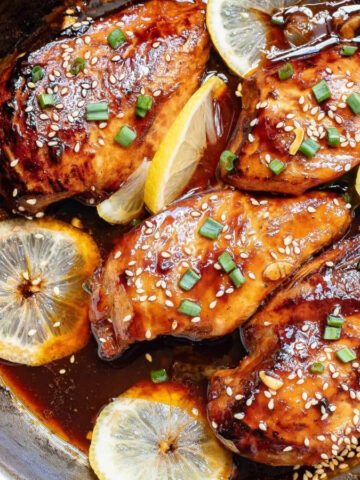 Asian glazed chicken in a skillet with lemon slices.