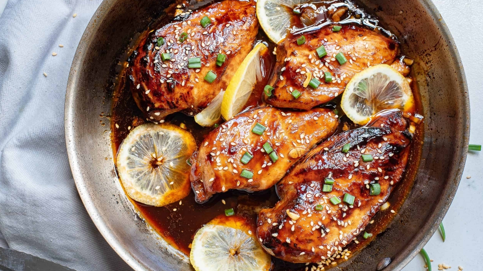 Asian glazed chicken in a skillet with lemon slices.