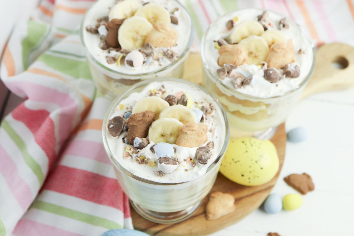 Finished Easter banana pudding parfait topped with whipped cream, bunny grahams, mini chocolate eggs, and banana slices.