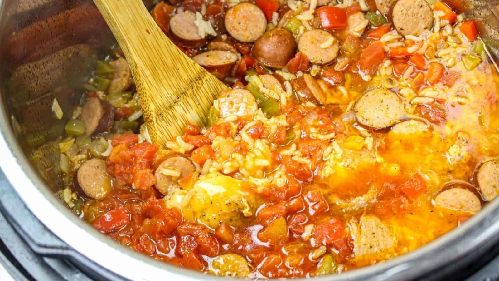 Chicken, sausage, and rice in instant pot with wooden spoon.