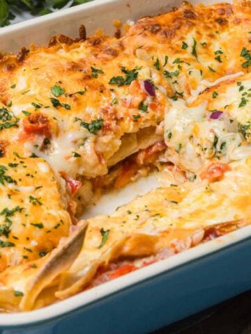 A cheesy baked lasagna in a blue dish, with a square piece removed and herbs sprinkled on top.