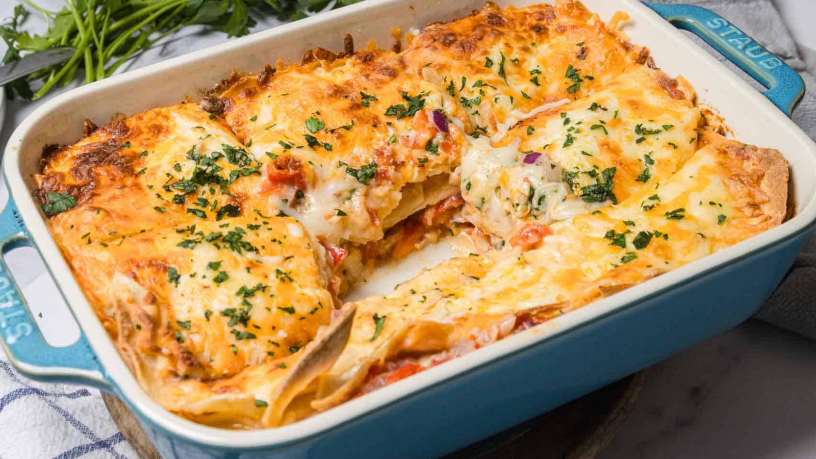 A cheesy baked lasagna in a blue dish, with a square piece removed and herbs sprinkled on top.