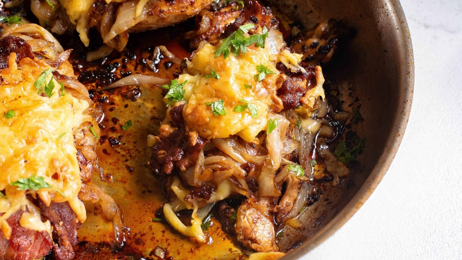 Chicken breasts in a skillet covered with onions and cheese.