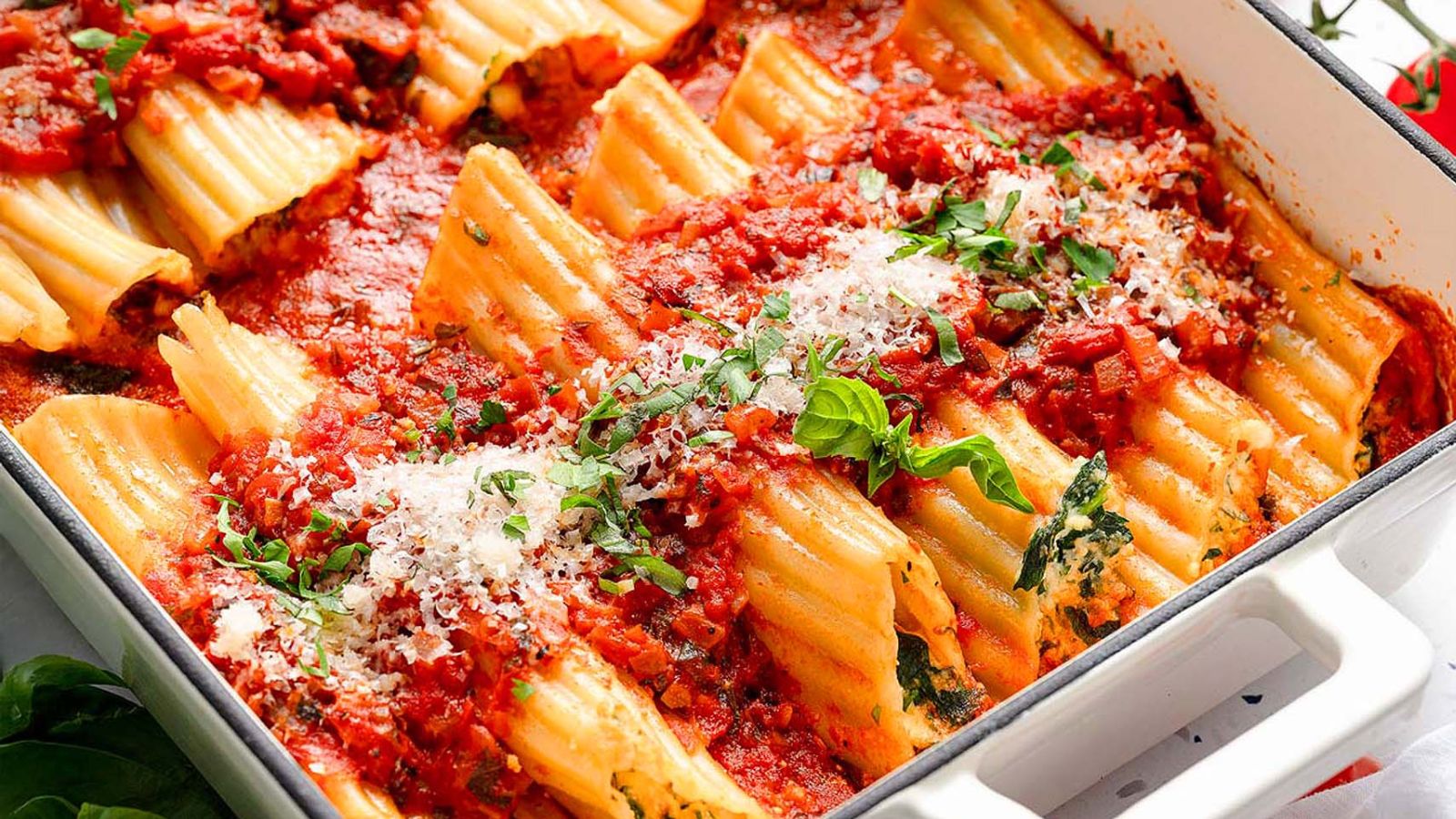 Spinach and cheese-stuffed manicotti pasta tubes arranged in a baking dish with red tomato sauce and grated cheese on top.