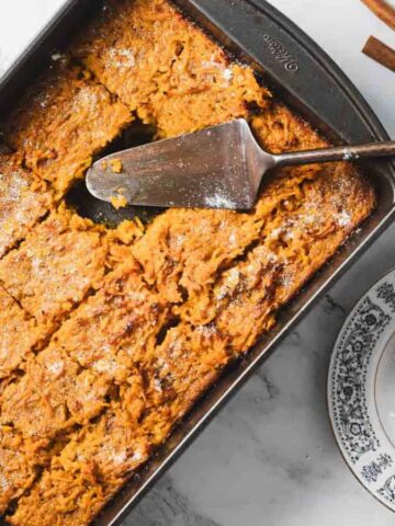 A delightful slice of carrot cake with a dollop of whipped cream graces a decorative black and white plate. A fork rests invitingly on the cake while a white and blue cup peeks from the background, almost like the perfect ending to a recipe for an unforgettable carrot casserole.